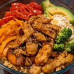 Yummy Bowl with jasmine rice, roasted sweet potatoes, broccoli, red bell peppers, grilled chicken, and tahini sauce, topped with avocado and green onions in a white bowl.