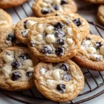 Cookies and Cream cookies freshly baked and cooling on a wire rack with visible chocolate sandwich cookie pieces and white chocolate chips.
